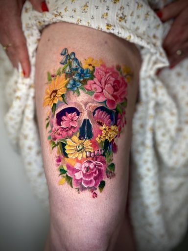 Colourful floral sugar skull thigh tattoo with vibrant pink, yellow and blue flowers in Lena Luna Tattoo signature watercolour style