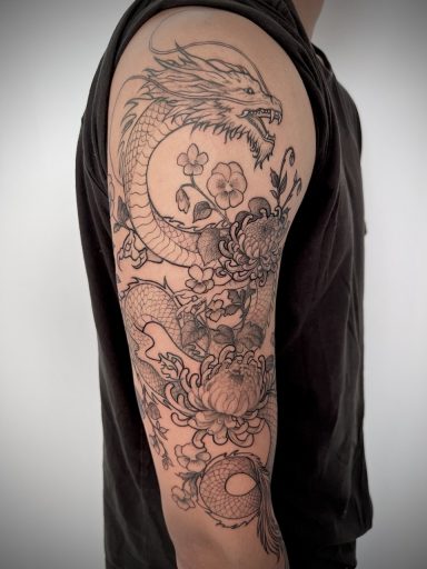 Fine line dragon and floral tattoo extending from the upper arm towards the elbow
