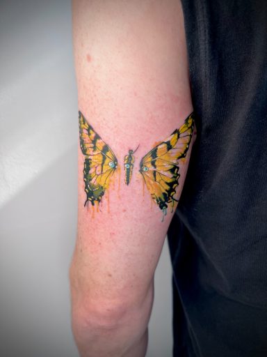 Yellow butterfly colour tattoo on upper arm with painterly effect and ink drops, by Letchworth tattoo artist