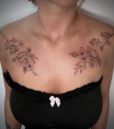 Symmetrical fine line floral tattoo extending across both collarbones and shoulders