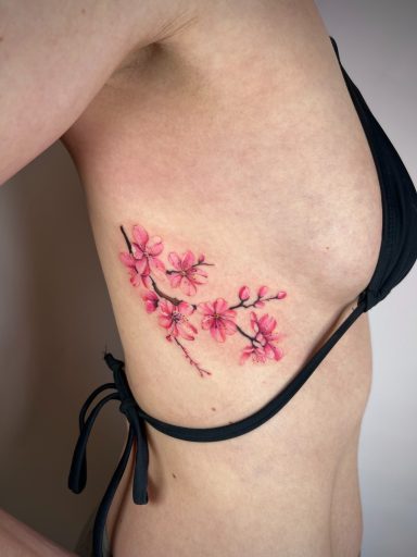 Pink cherry blossom branch tattoo on ribs with soft shading, colour floral tattoo by Letchworth artist