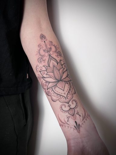 Ornamental fine line forearm tattoo featuring a lotus flower with detailed mandala patterns