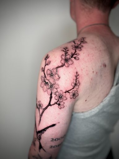 Fine line cherry blossom branch tattoo flowing across the shoulder and upper arm
