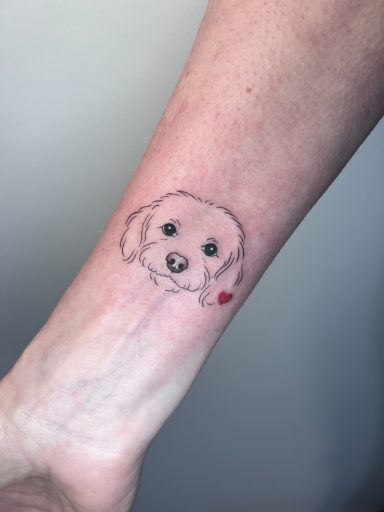 Minimal fine line dog portrait on wrist with small red heart detail, by Letchworth tattoo artist